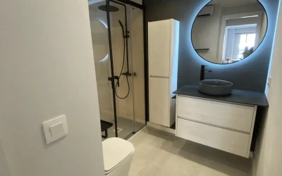 Baño moderno con ducha acristalada y espejo circular iluminad